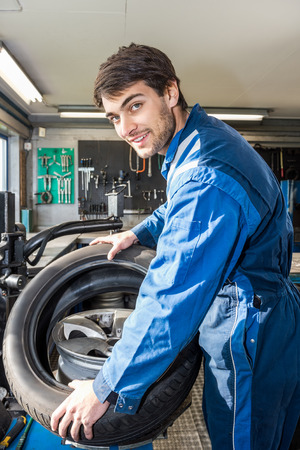 Portrait of confident male mechanic mounting car tire on rim in garageの写真素材