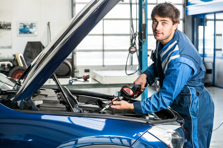 Portrait of male mechanic filling oil into car's engine at garageの写真素材