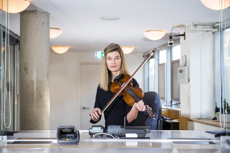 Classical Musician, playing a violin, sitting behind a counter at a ticket booth, selling ticketsの写真素材