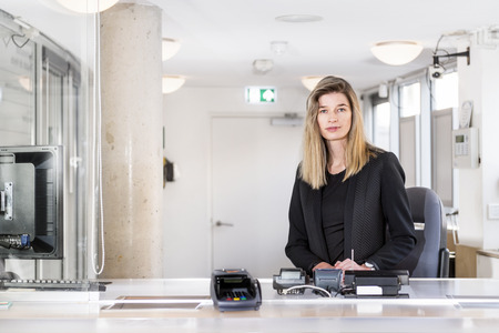 Sales woman, dressed in classy black, sitting behind the counter of a ticket booth in an officeの写真素材