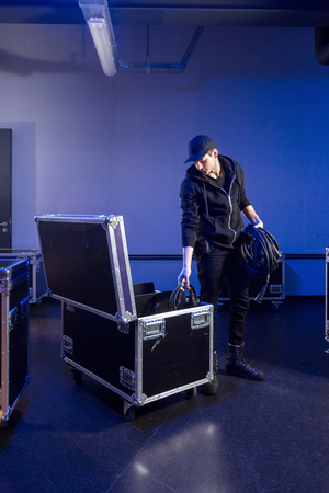 Roadie unpacking some high voltage power cables out of a flightcase, in preparation for a music concert at an event venueの写真素材