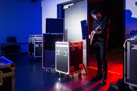Roadie playing guitar backstage, standing near the stage entrance, surrounded by flight cases, containing equipment.の写真素材