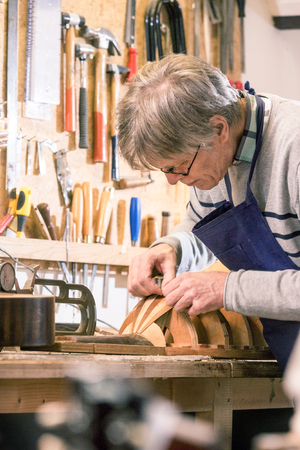 Luthier carefully carving the body shape of a lute, with an eye for detail, showing true crafsmanship, dedication, knowledge and passion for the instrument making trade.の写真素材