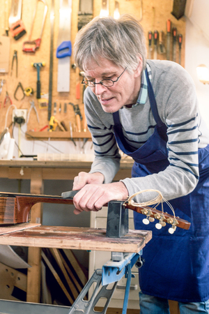 Guitar repairer filing the frets of an acoustic guitar on a workbenchの写真素材