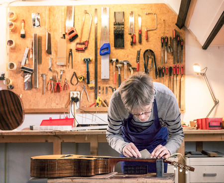 Luthier working on a workbench measuring and leveling the frets of a guitar with his tools in the backgroundの写真素材