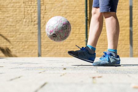 Boy keeping a ball up, wearing worn-down sneakers on a street soccer pitch
