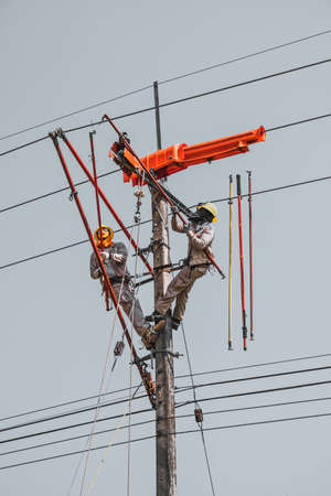 Two linemans use devices that are insulated for maintenance high voltage distribution system. To...