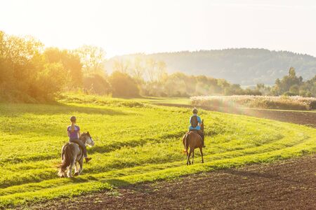 Two girls riding on their horses in beautiful afternoon sunlightの写真素材