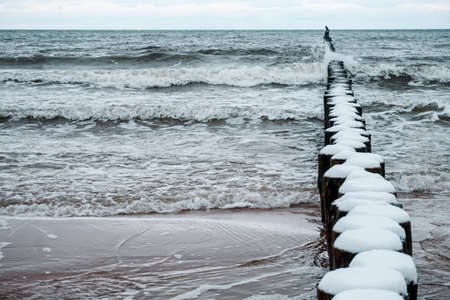 Wooden groyne on a beach covered with snow - winter time