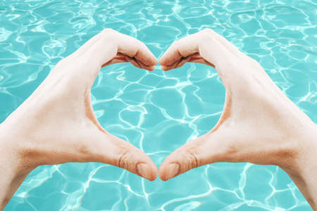 Hands forming heart shape, blue water surface - holiday conceptの写真素材
