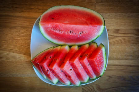 Cut watermelon on plate, wooden table - top view