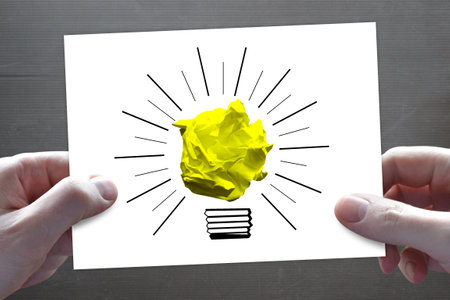 Hands holding paper with lightbulb drawn on it against grey backgroundの写真素材