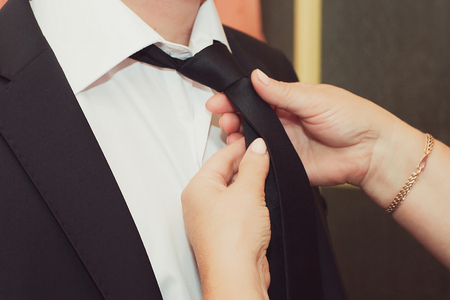 Mother helps her son groom attach the wedding boutonniere, closeup shot of handsの写真素材
