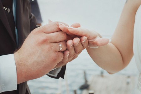 Hands with rings Groom putting golden ring on bride's finger during wedding ceremonyの写真素材