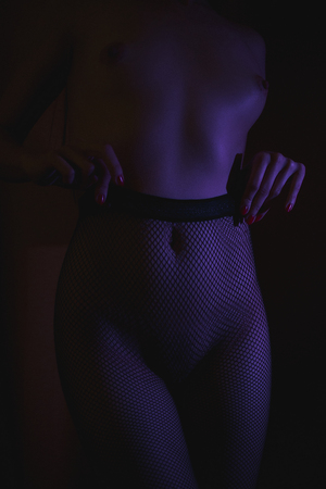 Crop shot of curvy female hips in fishnet tights standing in dark neon lightsの写真素材