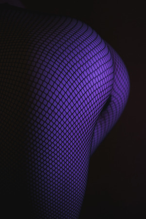 Back view of crop female with sexual ass in stockings in grid standing in darknessの写真素材