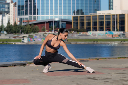 Attractive woman warming up and stretching before jogging on embankment