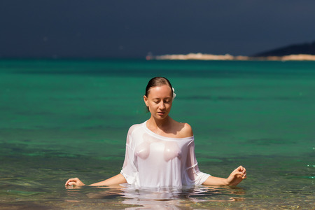 Sensual young female in wet blouse standing in clean sea water and looking awayの写真素材