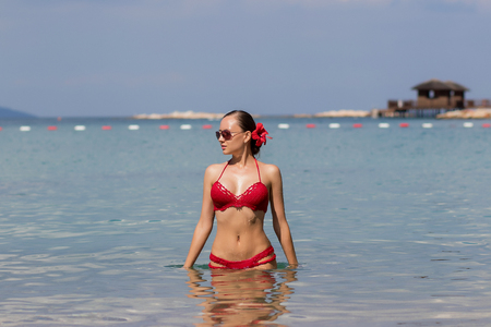 Beautiful woman walking in sea waterLovely young lady in red knitted swimwear looking away and walking in sea water while relaxing in wonderful resortの写真素材