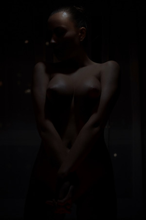 Crop attractive slim nude lady with closed eyes posing in dark room