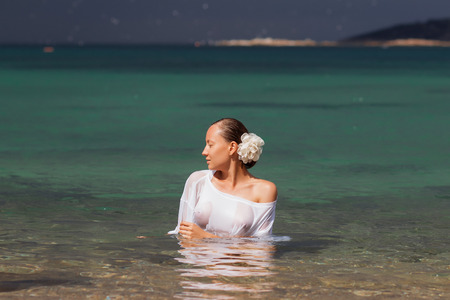 Sensual young female in wet blouse standing in clean sea water and looking awayの写真素材