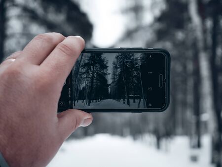 A man takes photos of the winter forest on his phone