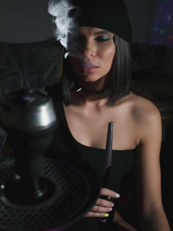 Brunette smoking hookah in dark roomの写真素材