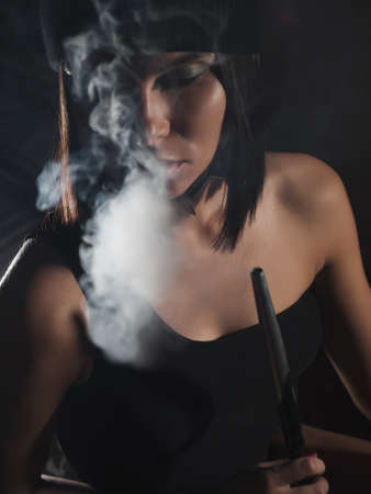 Brunette smoking hookah in dark roomの写真素材