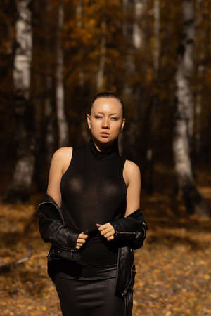 Seasonal autumn fashion. Modern young woman wearing fashionable warm clothes posing in the autumn park.の写真素材