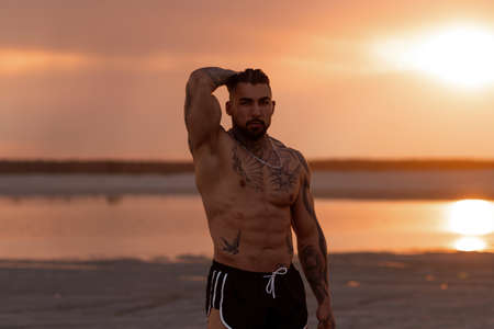 Handsome young muscular italian man posing shirtless on the beach, sunset summer time. Ideal fit body.の写真素材