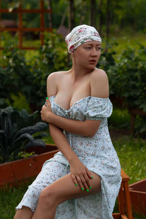 Full body of charming barefoot female in headscarf in dress with bare shoulders sitting with closed eyes in garden near green plants in countrysideの写真素材