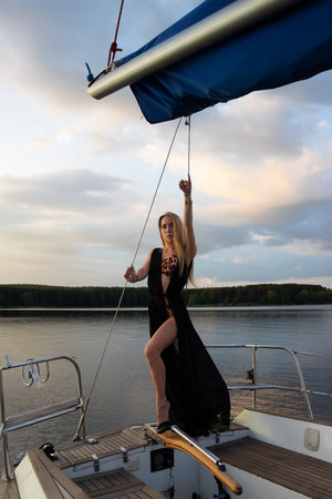 Gorgeous fit woman standing on yacht deck and admiring sea at sunsetの写真素材