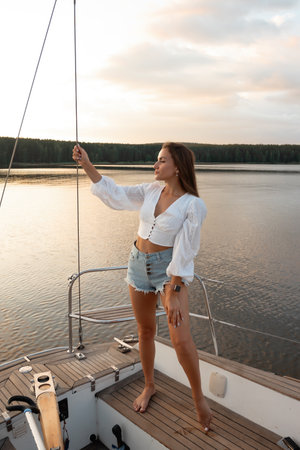 Gorgeous fit woman standing on yacht deck and admiring sea at sunsetの写真素材