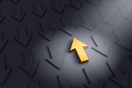 A spotlight illuminates a bright, gold up arrow on a dark gray background filled with down arrows.の写真素材