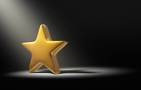 A spotlight brightly illuminates a single gold star on a dark background.の写真素材