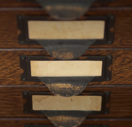 Stack of three old, oak flat file drawers with blank yellowed tags in tarnished brass label holders....