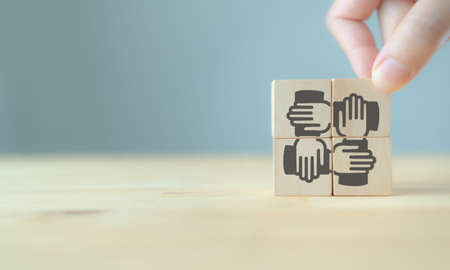 Hand pick up  wooden cube screening teamwork vector icon  standing on the wood table with blue background, copy space. Target for business management, teamwork, collaboration, achieve a common goalの写真素材