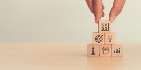 Business goal 2022. Hand pick up wood cubes with icon business strategy, action plan, goal, increase sale, process, game plan, copy space, blue background Business development Achieving business goal.の写真素材