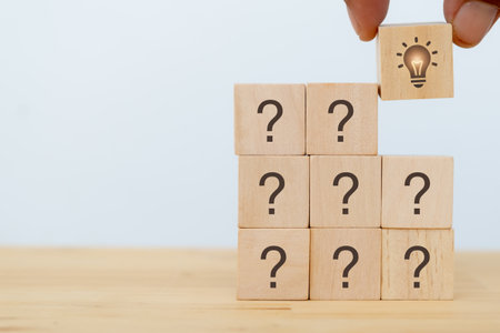 Creative idea, innovation and solution concept. Team brainstorming for problem solving. Hand puts wooden cubes with light bulb icon standing with question marks icons on white background, copy space.の写真素材