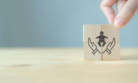 Child plan, life insurance concept. Family saving money for the future. Hand put  the wooden cube  with hand holding child symbol on beautiful grey background, copy space. Child insurance banner.の写真素材