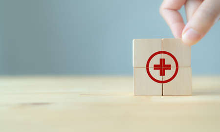 Health and medical treatment concept. The doctor puts the wooden cube with medicine cross sign standing on table and blue background with copy space. Use for banner in healthcare and medical business.の写真素材