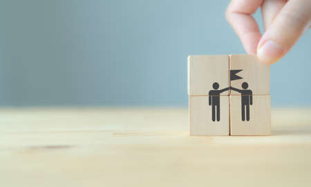 Business success and goal achievement concept with unity and teamwork.  Businessman hold wooden cubes with wining team icon on beautiful grey background, copy space. Banner for winner and leader.の写真素材