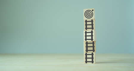 Business goal success concept. rises up Stairs to goal and achieve successful business. Initiation for planning to reach target. Darts target aim icon on wooden cubes with grey background. Copy spaceの写真素材