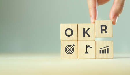 OKR text (Objectives, Key and Results) wooden cube blocks on blue background. Business target and drive business and performance. Focus on goal. Achieve business growth by flexible managementの写真素材
