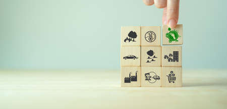 Carbon footprint, low carbon emission concept. Climate changing problems solving goals. Stacking wooden cubes with carbon footprint icon on pollution source icons on grey background,copy space. LCA.の写真素材