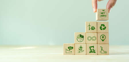 Net zero and carbon neutral concept. Net zero greenhouse gas emissions target. Climate neutral long term strategy.  Stacking wooden cubes with green net zero and save world icon on grey backgroud.の写真素材