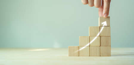 Growth and success concept.  Business common goals and strategies. Hand puts wooden cubes  with growth trend performance on grey background and copy space. Banner for new action plan ,goals, success.の写真素材