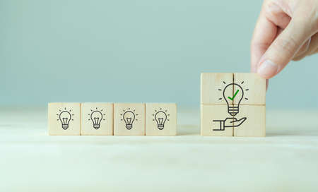 Suggestion and consulting concept. New idea, solution. Putting wooden cubes with light bulb on hand icon on beuatiful grey background and copy space. Business review, strategy suggestion for businesの写真素材