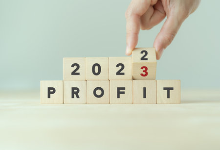 Business profit plan concept in 2023 . Build a profit and financial plan. Hand flip wooden cubes 2022 to 2023 with text "PROFIT" on grey background and copy space. Business performance target in 2023の写真素材