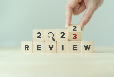 2023 Review concept. For business planning. Hand flips a wooden cube and changes the inscription 'Review 2022' to 'Review 2023'. Beautiful grey background, copy space. Successful resolution strategy.の写真素材
